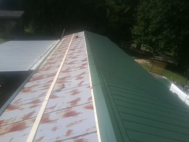 Old rusted panels beside newly installed green metal roofing — Wind Damage Roof Repair by Roofing Brothers in Mayville