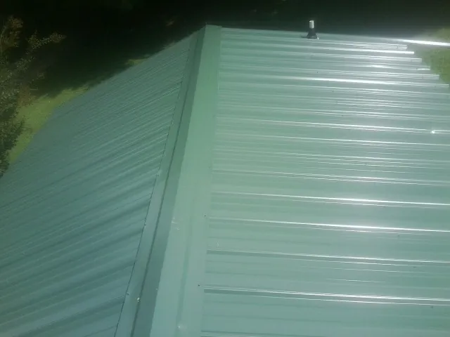 New green metal panels meeting at the ridge of a roof — Flat Roof Repair work by our crew in Mayville