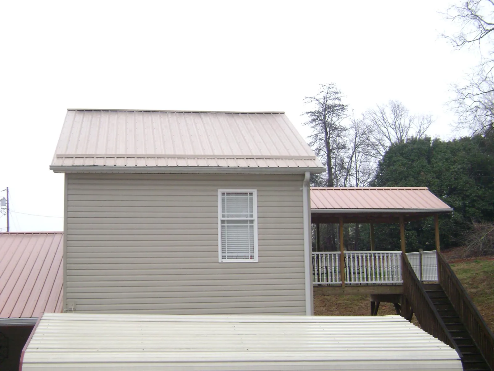 Tan metal roofs on a two story addition and attached porch, from a Roof Replacement job in Mayville